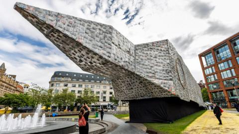 Marta Minujin's Big Ben Lying Down With Political Books in Manchester's Piccadilly Gardens