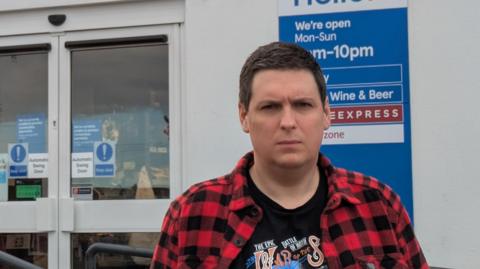 Man stands in front of shop.