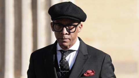 Jay Blades in a black cap and black jacket 