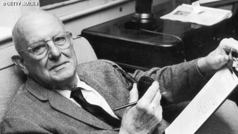 PG Wodehouse sits in a chair with a clipboard and a pipe