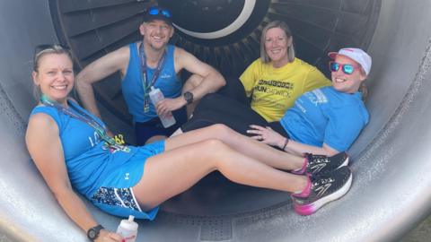 Four people sitting in a plane engine. Two with their medals