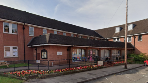 The outside of Lichfield District Council. It is a red brick, two-storey building with multi-coloured flowers along the front