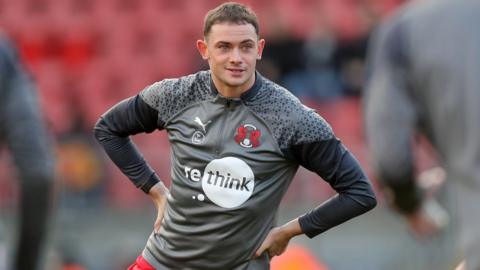 Theo Archibald, wearing a grey Leyton Orient training top and red shorts, with his hands on his hips
