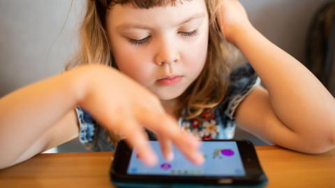 A young girl plays with a computer tablet on a table