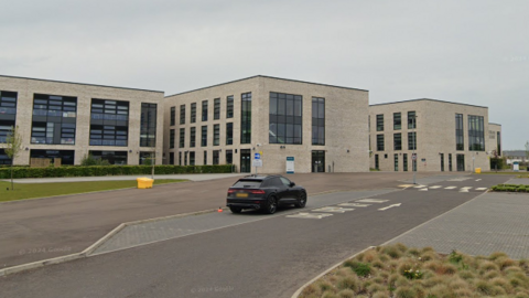 A modern, pale stone secondary school building with drop-off car bays in front.