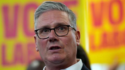 Sir Keir Starmer pictured wearing a dark suit with Labour placards in the background