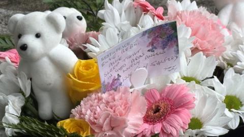 White teddy bears with white, pink and yellow floral tributes at Southport.