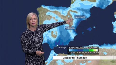 Sarah Keith-Lucas standing in front of a weather map showing rainfall accumulation in Spain