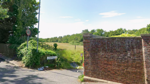A Google Street View shot of the junction where the incident took place. The main road is a busy tree-lined 40 mile per hour road with cars on it and the lane is a narrow 20mph road with a field to the side