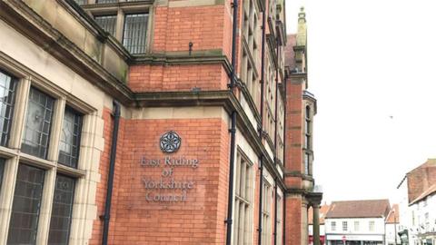 Exterior of the Guildhall in Beverley - a red brick building with mullioned stone windows and the East Riding of Yorkshire Council name and white rose logo on the side