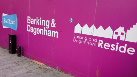 Bright magenta hoarding along a pavement displays Barking and Dagenham branding, including Be First and B&D Reside logos with simple house icons. 
