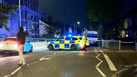 A police cordon and a blue and yellow police car seen 