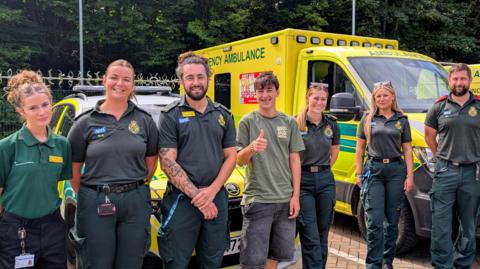 A teenager with six paramedics stood in front of an ambulance.
