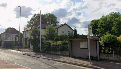 Carters Arms on Manchester Old Road Middleton is obscured by trees, a lampost and phone mast. There is a buys shelter and stop to its left.