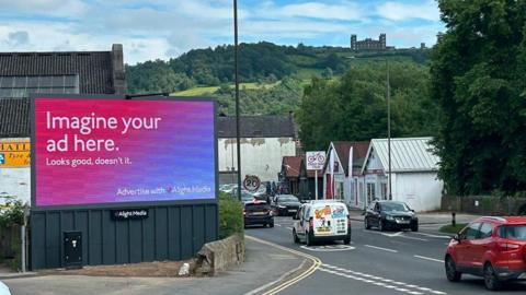 Large digital advertising billboard on the edge of a junction with a rural hillside backdrop