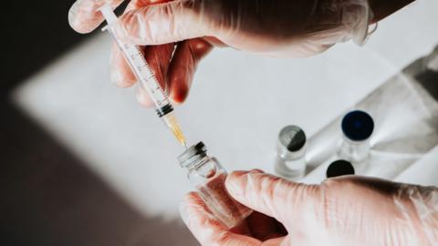 A person loads a syringe with a vaccine in a small glass jar.
