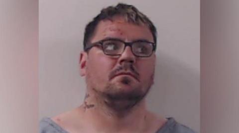 Gordon Docherty is pictured in a police mugshot. He has short dark hair, stubble and is wearing glasses. He is looking off to the right.