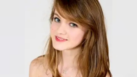 Alice smiles at the camera. She is a young woman with long dark hair, and wears a delicate silver necklace and light pink lipstick.