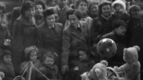 A crowd of women and children look at toys through a window.