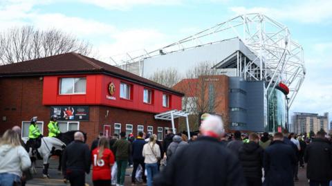 Manchester United fans walk to Old Trafford as mounted police watch on outside the football club.