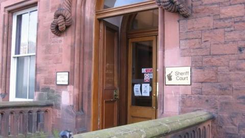 The sandstone court building at Dumfries with wooden doors and a brass panel with the words Sheriff Court on it