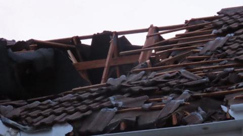 A picture of a damaged roof. There is a number of panels missing, with wooden structure showing.