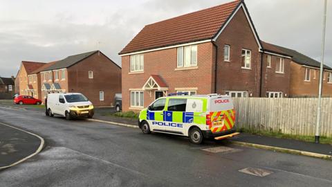 Police van outside a modern red-brick house.