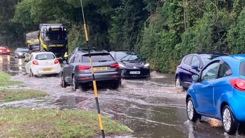 Cars drive through flood water on a busy road. 