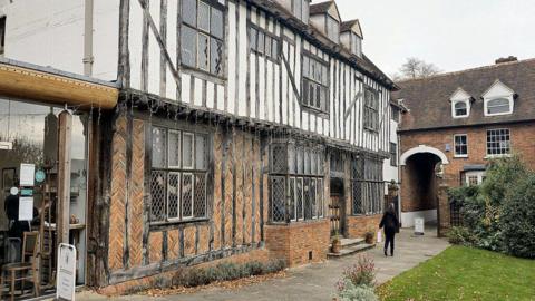 The frontage of Tymperleys, a 15th Century building in Colchester city centre. It is a half white, half brick building with black wooden beams.