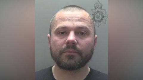 Police custody photograph of Radoslaw Golec. He has short dark hair and beard and is wearing a black shirt.