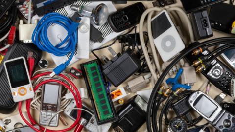 A pile of old mobile phones, wires and plugs