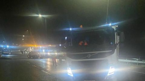A picture taken in darkness shows a number of pieces of machinery including large lorries and diggers with their lights on on what appears to be a section of motorway