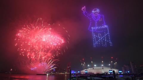 Drones form the image of Captain Tom above the O2 while fireworks glow red above the River Thames.