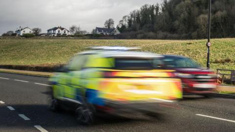 A speeding police car in the left lane, which is blurry, with a car in the other lane also blurry in the next lane driving in the opposite direction.