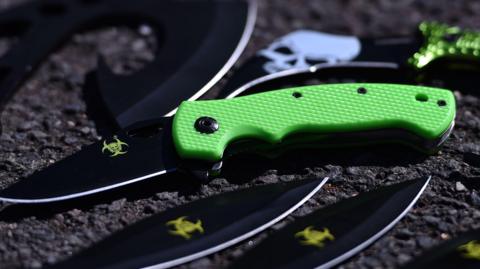 Examples of zombie knives - one with a bright green handle - laid out on a table 