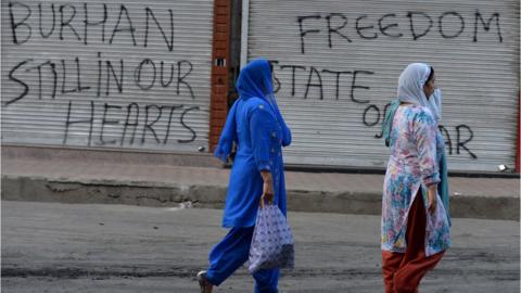 Women walk past a shuttered shop with pro-militant slogans spray painted on