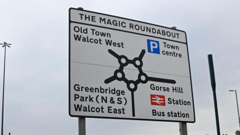 Directional sign of Swindon's Magic Roundabout showing the routes to the town centre, the Old Town Walcot West, Greenbridge Park and Gorse Hill railway station