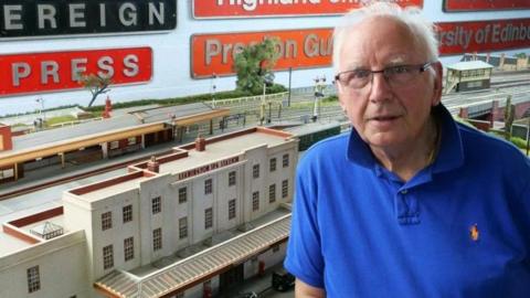 A man in a blue polo shirt in front of a model railway.