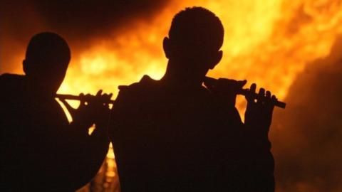 Flautists playing beside a bonfire