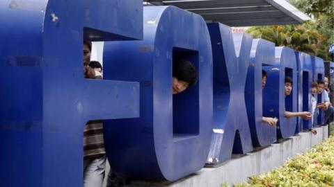 Workers standing behind a giant Foxconn sign