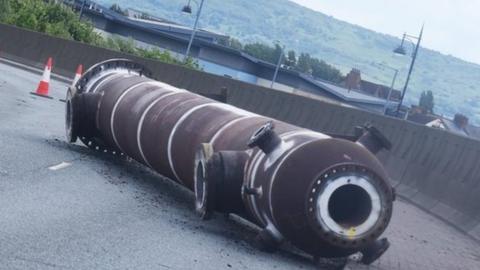 A large metal pipe lies on the road