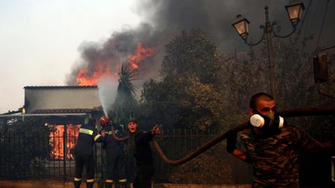 Firefighters and volunteers battle to put out a fire burning a house in the residential area of Kryoneri, in the suburbs of Athens