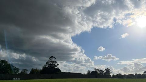 Partly cloudy skies over grassland with houses in the distance 