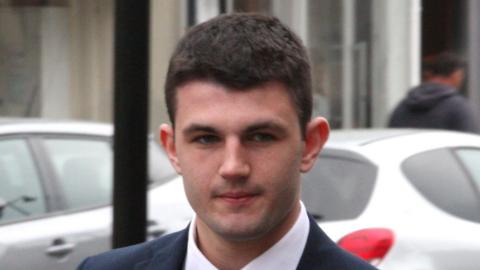 A young man with dark hair wearing a suit is pictured outside