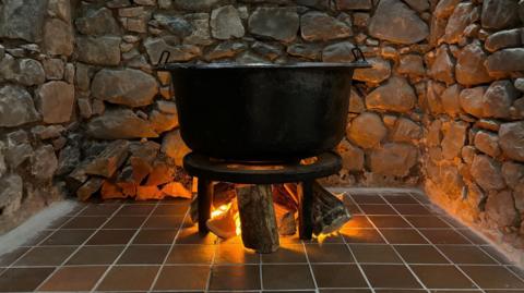 A cast iron post resting above burning wood on a tile floor surrounded by stone wall. 