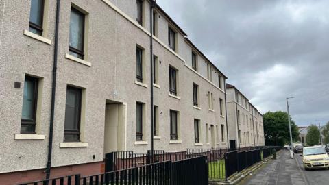 Street view of pebble-dash flats behind a black iron fence