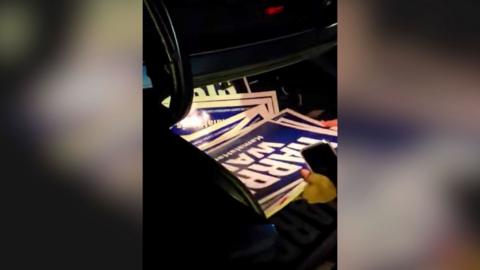 Harris/Walz campaign signs are seen being removed from a car boot.