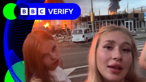 Two Russian women appear in a social media video with a fuel depot on fire behind them