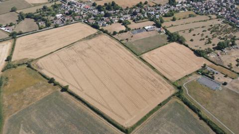 An aerial view of the village of Keinton Mandeville surrounded by yellow-brown barley fields.