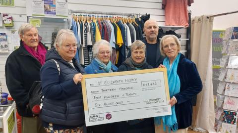 Six people are standing in a row holding up a giant cheque to St Elizabeth Hospice 